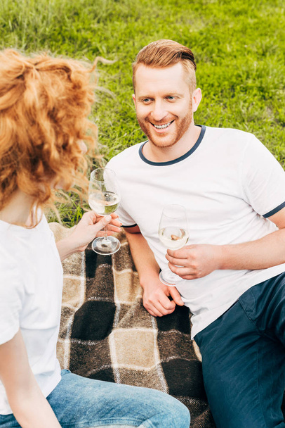 hoge hoekmening van gelukkig rdhead paar drinken van wijn op picknick in het park - Foto, afbeelding