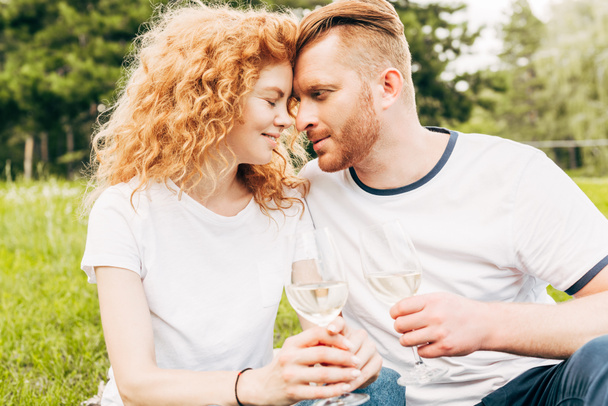 happy couple touching foreheads while drinking wine at picnic in park - Foto, afbeelding