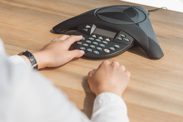 Oříznout záběr podnikatelka mačkání tlačítka konferenční telefon na stole v kanceláři - Fotografie, Obrázek