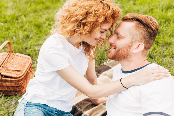 vista lateral de feliz pelirroja pareja sonriendo juntos en el picnic en el parque
 - Foto, imagen