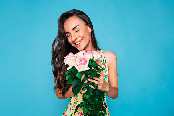 Young smiling woman in colorful swimsuit posing with bouquet of roses on blue background - Fotografie, Obrázek