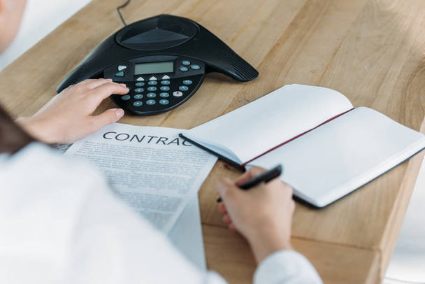 обрезанный снимок предпринимательницы с контрактной кнопкой конференц-телефона на столе в офисе
 - Фото, изображение