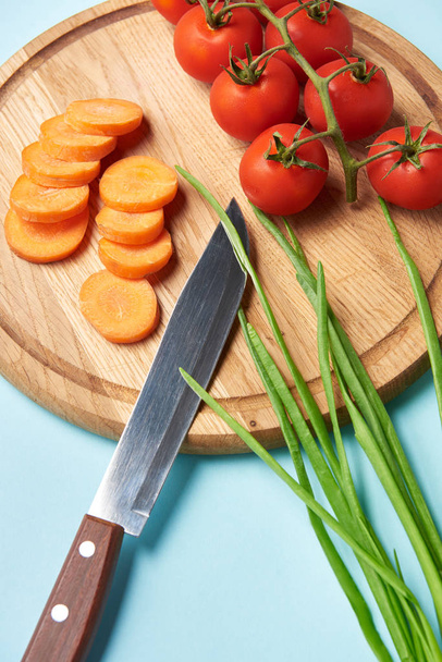 close up view of knife and assorted fresh vegetables on wooden cutting board on blue background - Photo, Image