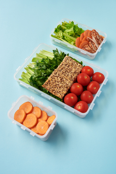 vista de cerca de la disposición de recipientes de alimentos llenos de verduras saludables, rebanadas de carne y galletas en el fondo azul
 - Foto, imagen