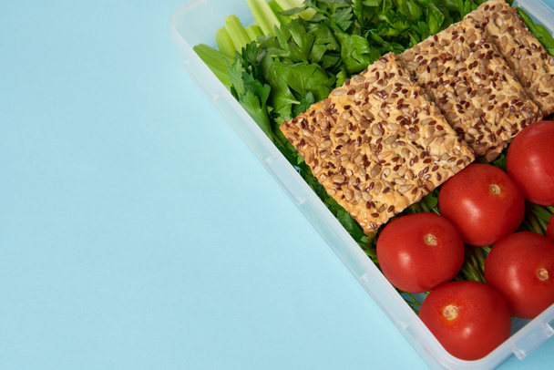 vista de perto do recipiente de alimentos cheio de vegetais saudáveis e biscoitos isolados em azul
 - Foto, Imagem