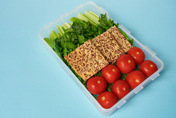 Nahaufnahme von Lebensmittelbehältern voller gesundem Gemüse und Keksen mit Samen vor blauem Hintergrund - Foto, Bild