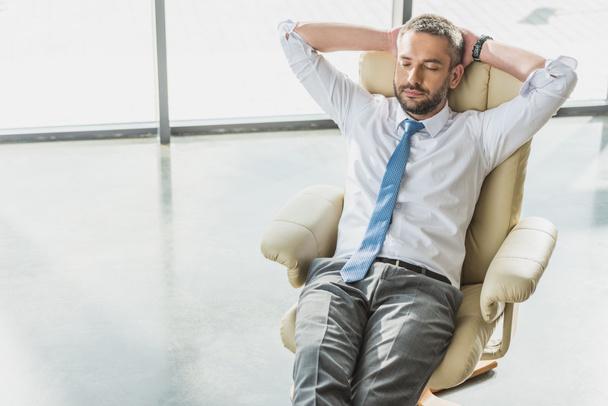 vysoký úhel pohled pohledný podnikatel relaxační na luxusní křeslo v moderní kanceláři - Fotografie, Obrázek