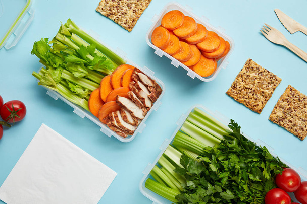 Ansicht der Anordnung von Lebensmittelbehältern mit frischen gesunden Lebensmitteln, Serviette und Besteck isoliert auf blau - Foto, Bild