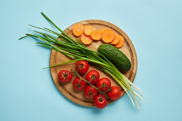 top view of assorted fresh vegetables on wooden cutting board isolated on blue - Foto, immagini