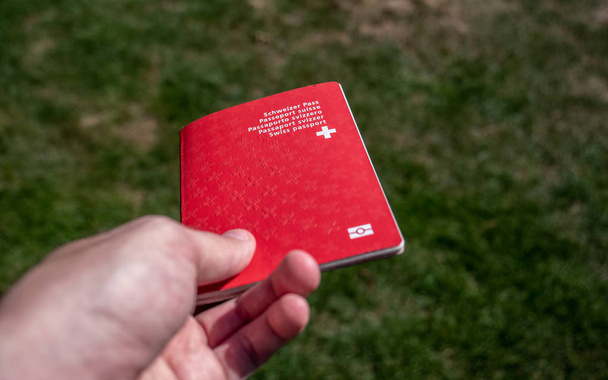 person holding the swiss passport on a sunny day grass background - Photo, Image