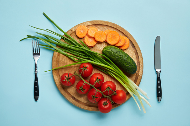 top view of cutlery and assorted fresh vegetables on wooden cutting board isolated on blue - Φωτογραφία, εικόνα