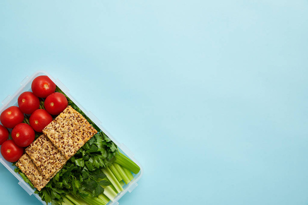 bovenaanzicht van voedsel container vol gezonde maaltijd met groenten en cookies geïsoleerd op blauw - Foto, afbeelding