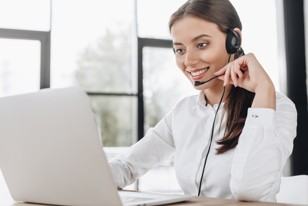 Krásné ženské call centrum pracovníka se sluchátky a laptop sedí na pracovišti - Fotografie, Obrázek