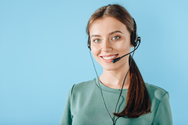 atractiva sonriente trabajadora del centro de llamadas mirando la cámara aislada en azul
 - Foto, Imagen