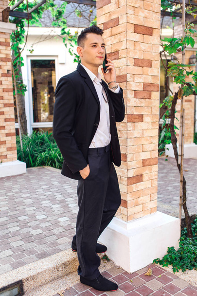 Young stylish handsome man posing in modern city park, wearing suit and sunglasses. - Foto, Imagen