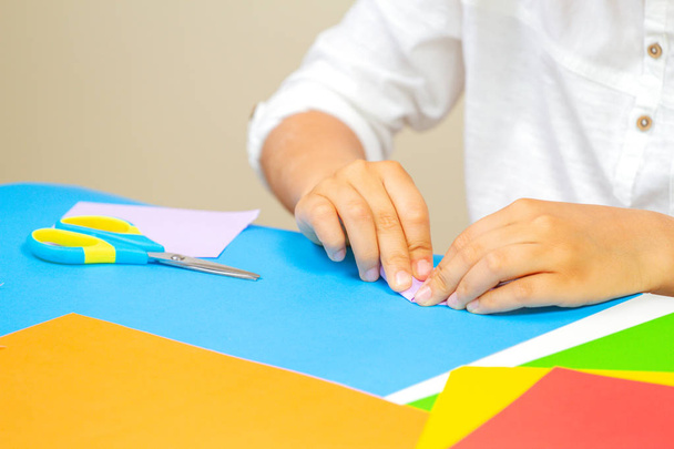 Ręce dzieciak Dokonywanie kartkę z życzeniami z kolorowego papieru na stole - Zdjęcie, obraz