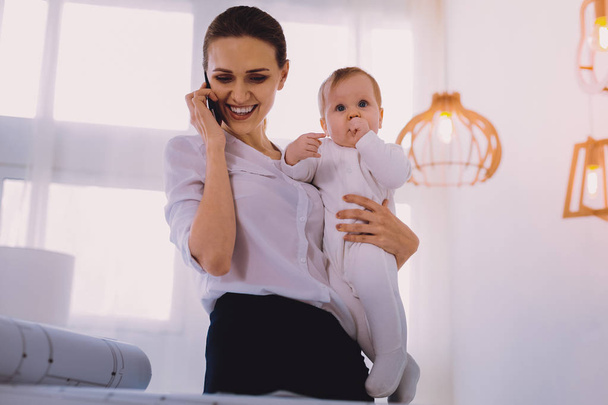 Positive engineer talking on the phone while staying at home with baby - Fotoğraf, Görsel