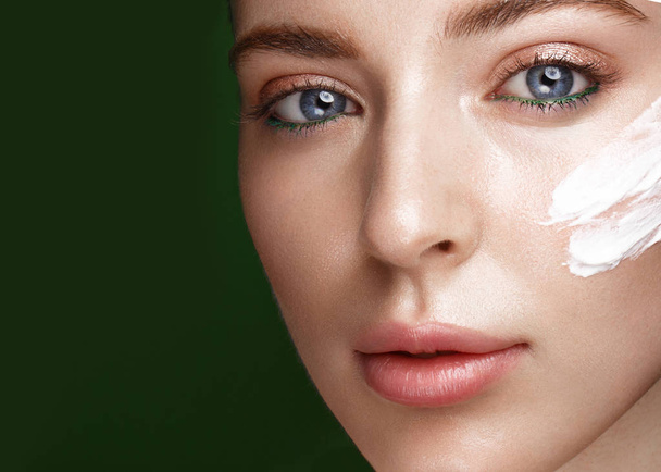 Beautiful fresh girl with cosmetic cream on the face, natural make-up and green leaves. Beauty face. - Foto, imagen