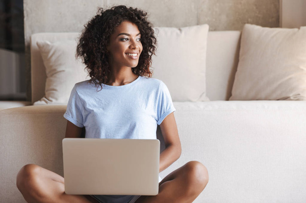 Happy african woman using laptop computer while sitting at a couch at home - Φωτογραφία, εικόνα