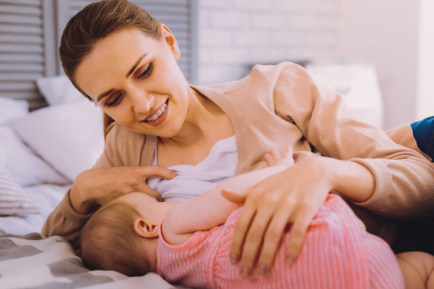 Smiling woman breastfeeding the baby and looking pleased - Fotó, kép