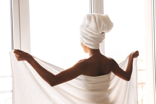 Back view of an attractive african woman wrapped in a towel standing in front of the wondow - Foto, Imagen