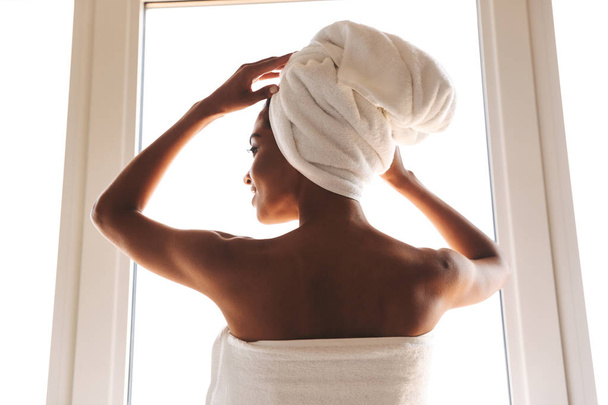 Back view of a sensual african woman wrapped in a towel standing in front of the wondow - Foto, imagen
