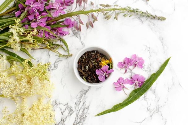 Porcelain Cup with dry herbal Ivan-tea with Fireweed and Meadowsweet on the marble table. Harvesting. - 写真・画像