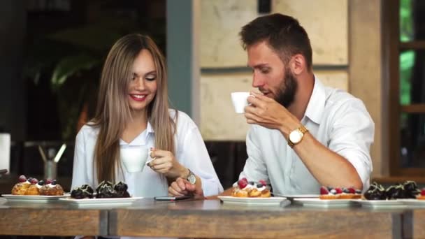 幸せなカップルのコーヒー ショップでスマート フォンのライン上のメディア コンテンツをみんなで共有 - 映像、動画