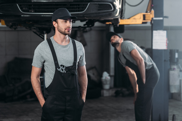 auto mechanic in overalls with colleague working in workshop behind - Zdjęcie, obraz