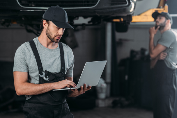 auto mechanic using laptop, while colleague working in workshop behind - Photo, Image