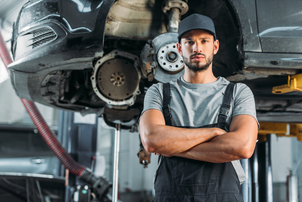 confident mechanic posing with crossed arms in auto repair shop - Foto, imagen