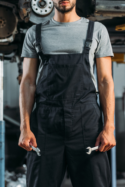 Ausgeschnittene Ansicht eines professionellen Automechanikers mit zwei Schlüsseln in der Werkstatt - Foto, Bild