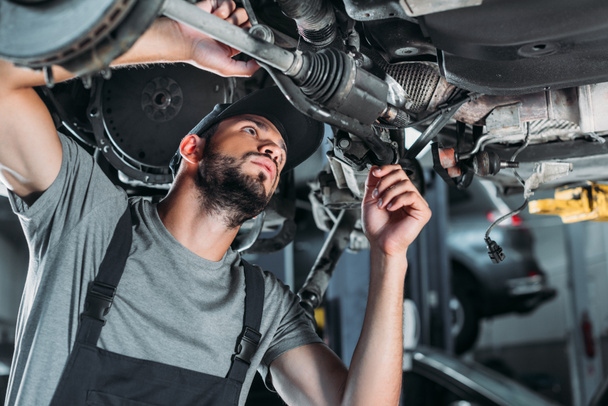 Mechaniker in Overalls repariert Auto in Autowerkstatt - Foto, Bild