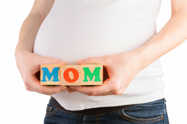 Pregnant woman belly with hands holding colorful wooden blocks with mom sign - Photo, Image