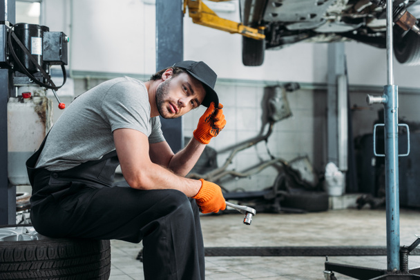 mechanic holding tool and sitting in auto repair shop - Foto, Bild
