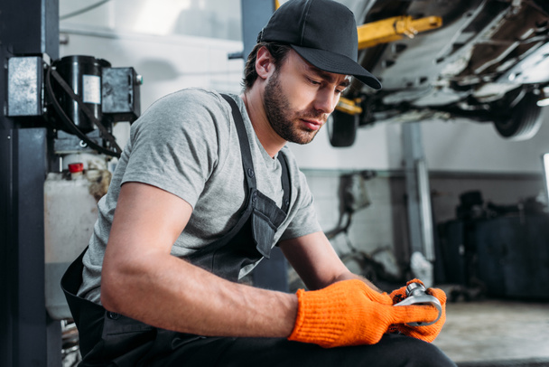 auto mechanic looking at wrench and sitting in repair shop - Valokuva, kuva