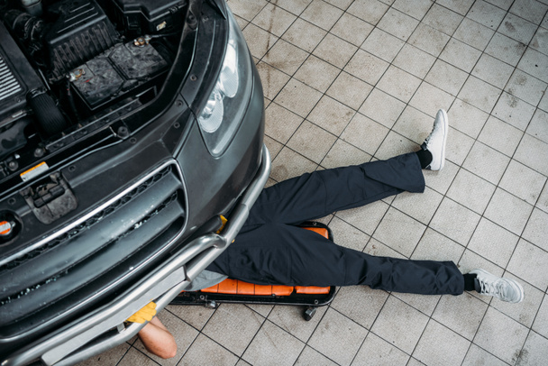 top view of mechanic lying and working under car   - Foto, Imagem