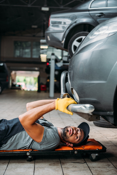 workman lying and working under car in mechanic shop - Foto, Bild