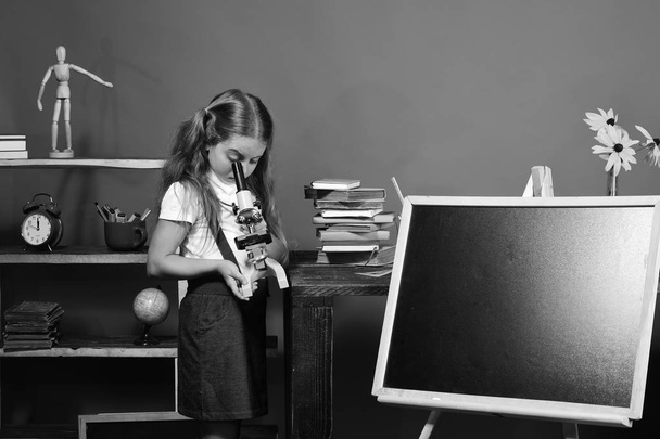 Schoolgirl with busy face in classroom. Girl looks into microscope - Valokuva, kuva