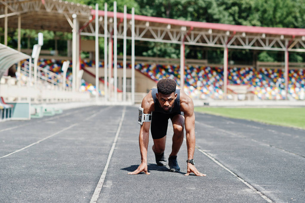 African american male athlete in sportswear racing alone down a running track at stadium. - Фото, изображение