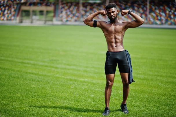 African american male athlete sexy sport bare torso man with running sports arm case for mobile phone, posed at green grass of football stadium. - Fotografie, Obrázek