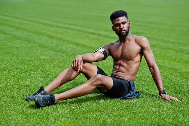 African american male athlete sexy sport bare torso man with running sports arm case for mobile phone, posed at green grass of football stadium. - Foto, immagini