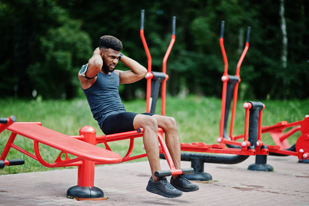 African american male athlete sport man with running sports arm case for mobile phone, doing exercises on the street workout simulators. - Фото, изображение