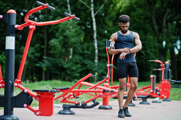 African american male athlete sport man with running sports arm case for mobile phone, posed against street workout simulators. - Foto, Imagem
