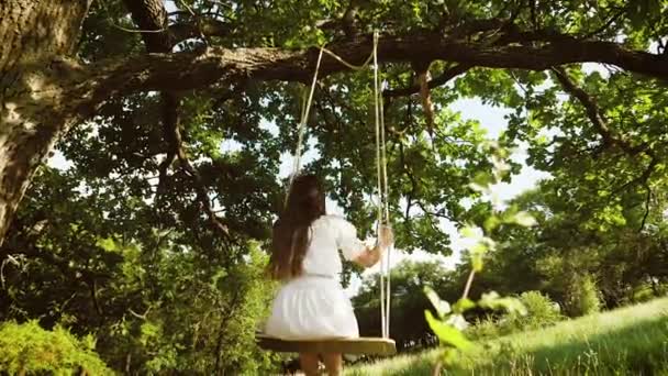 piękna dziewczyna z długimi włosami w białej sukni, kołysanie na swing w parku lato. Zwolnionym tempie. - Materiał filmowy, wideo