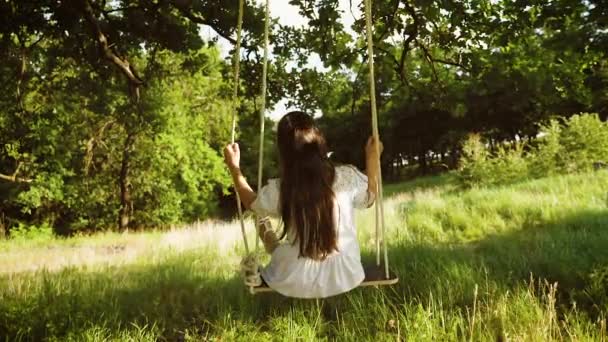 Dziewczyna z długimi włosami w białej sukni, kołysanie na swing w parku lato. Zwolnionym tempie. - Materiał filmowy, wideo
