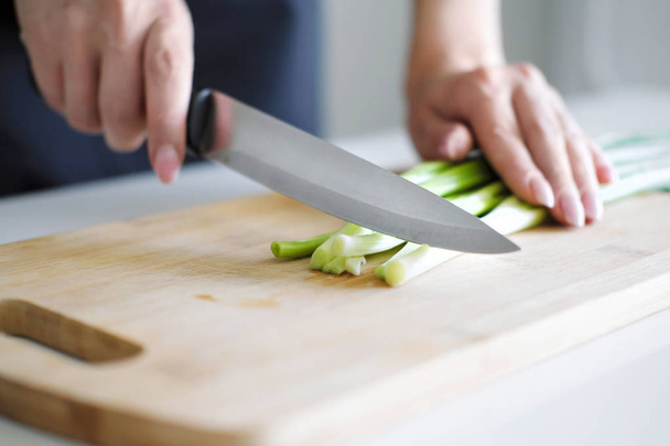 Female hands with a knife, slicing vegetables on a wooden board on a white background. - Valokuva, kuva