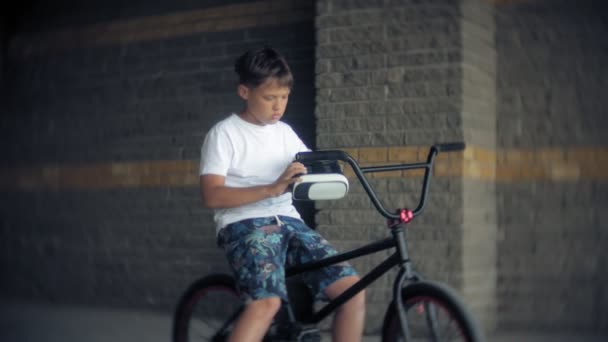 The boy is sitting on the ladder in virtual glasses, next to the bicycle BMX - Кадри, відео