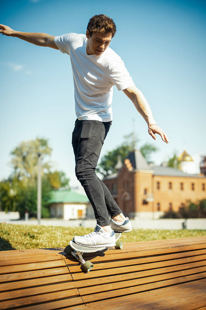 Young attractive man in white T-shirt riding longboard in the park. - Foto, Bild