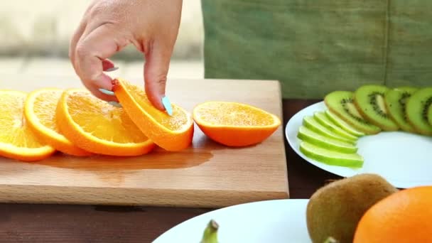 Vegetarian diet. A woman puts pieces of orange on a plate, which is on a cutting board. Full Hd shot with dolly from left to right. - Video, Çekim